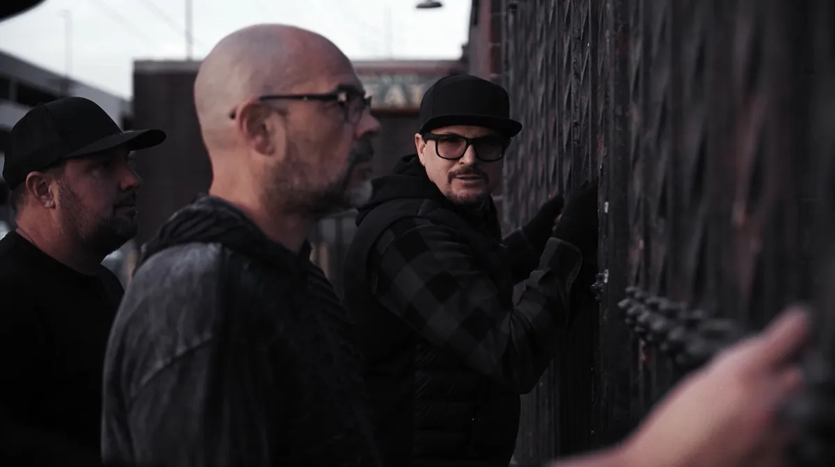 Zak Bagan in a black hat standing by a fence with Aaron Goodwin in the foreground
