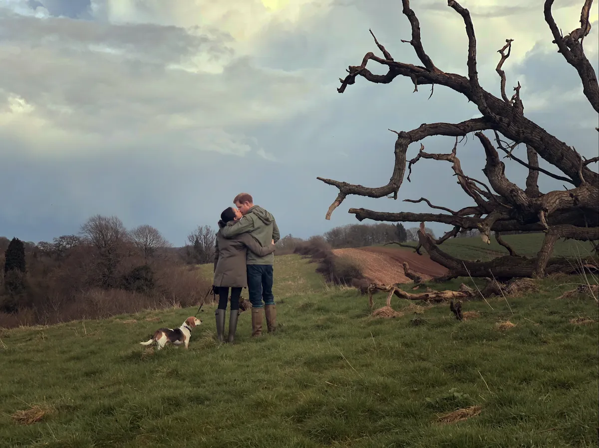 Meghan Markle and Prince Harry with their arms around each other and their backs to the camera standing on a grassy English landscape