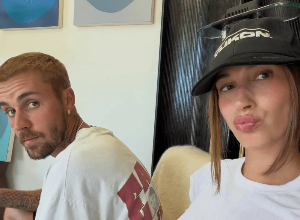 Justin and Hailey Bieber wear white shirts. She wears a baseball hat.