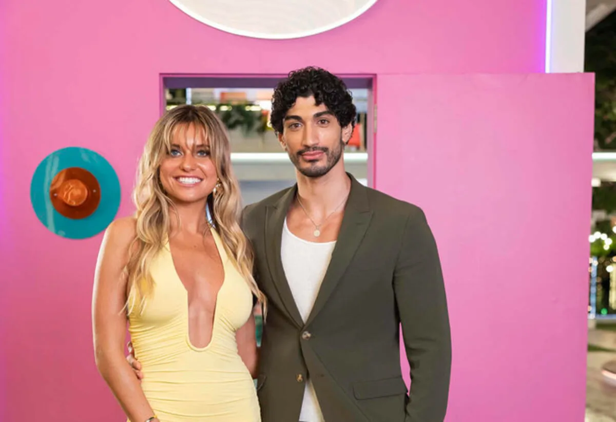 Kenzie Annis wears a yellow dress and stands with Zach Georgiou in front of a pink wall.