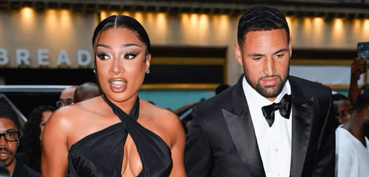 Megan Thee Stallion wears a black dress and walks with Klay Thompson, who wears a tuxedo.