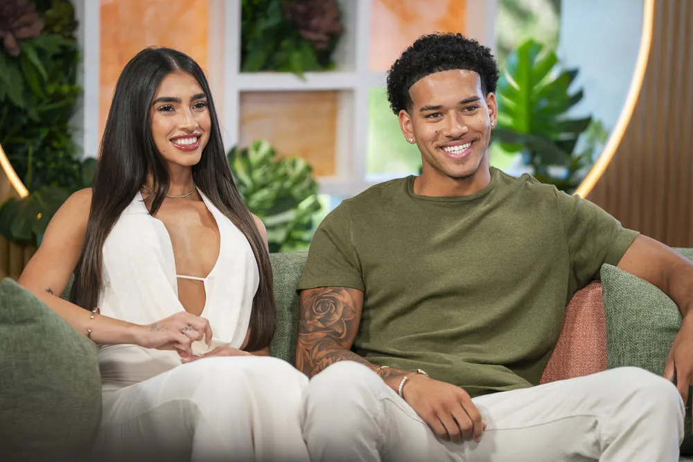 Parmida and Corbin sit next to other on a couch. Parmida wears white and Corbin wears green.