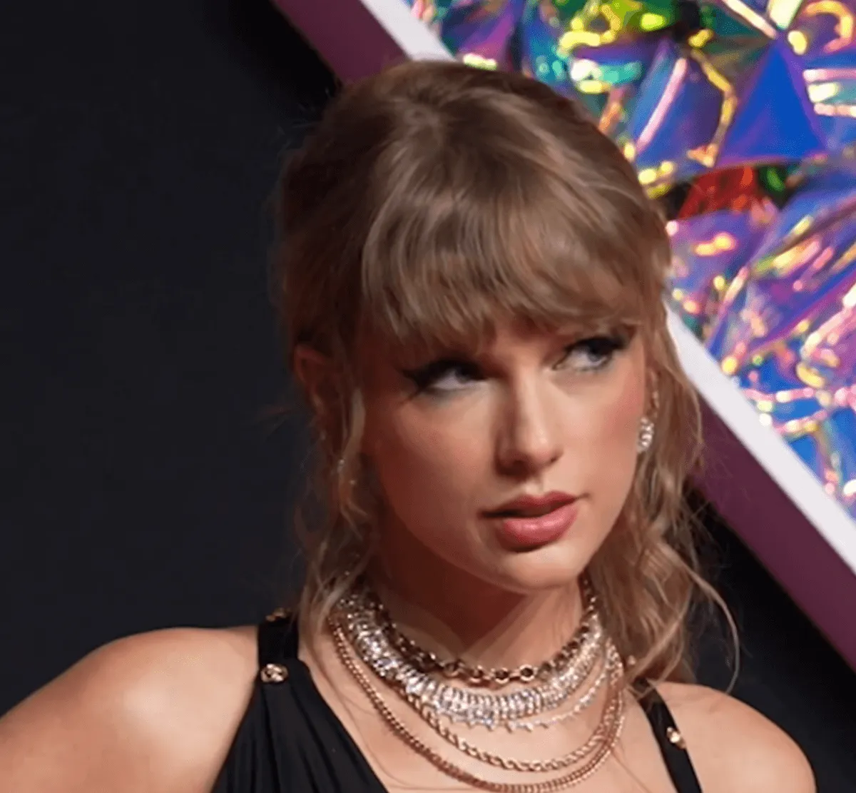 Taylor Swift wears a black dress and multiple necklaces.