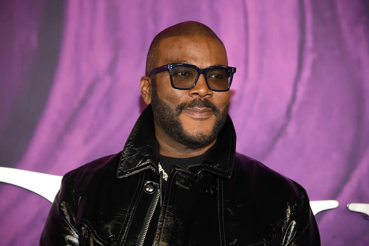 Tyler Perry wearing glasses standing in front of a purple background