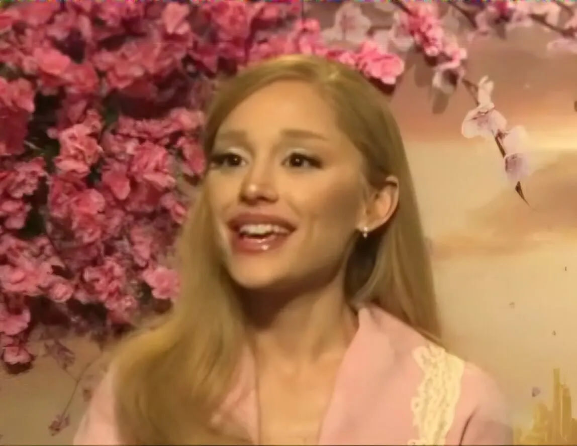 Ariana Grande wears pink and sits in front of pink flowers.