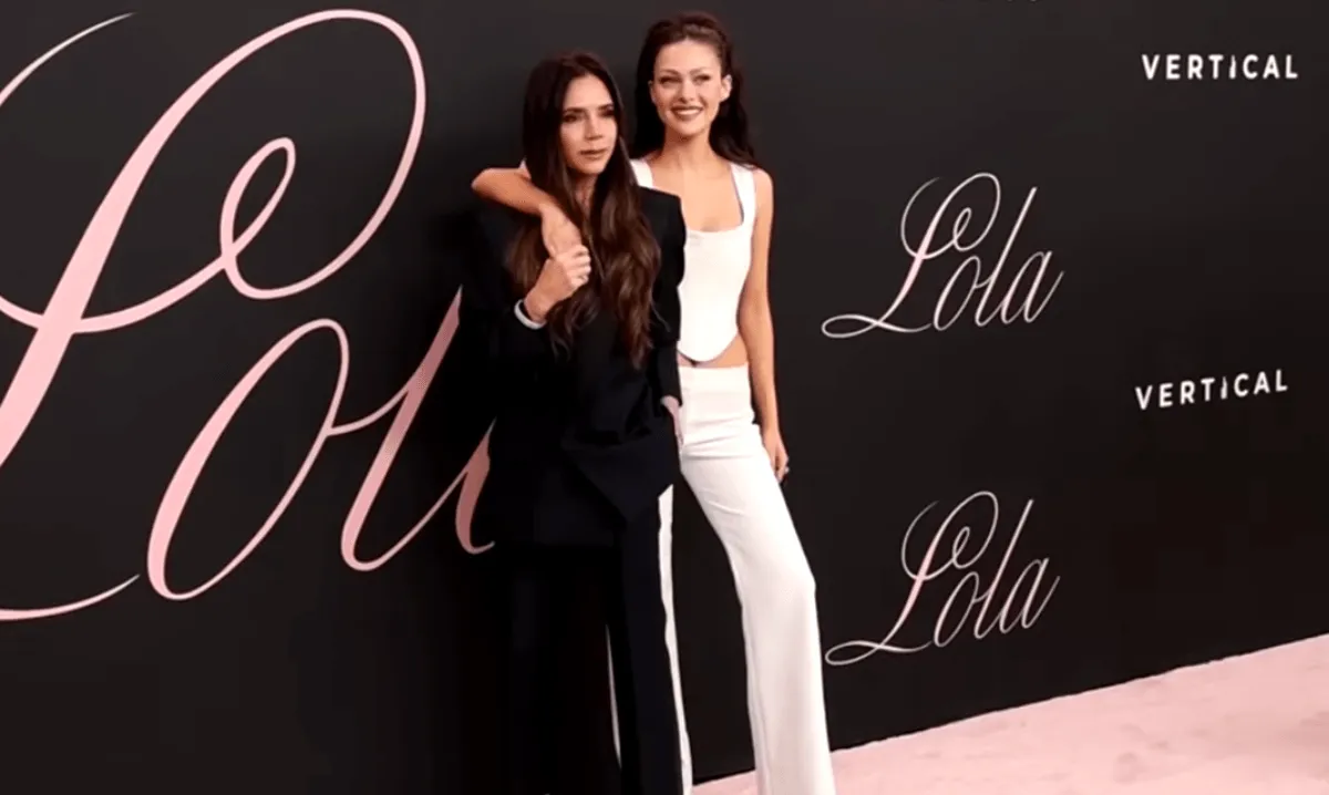 Victoria Beckham wears black and stands with Nicola Peltz, who wears white.