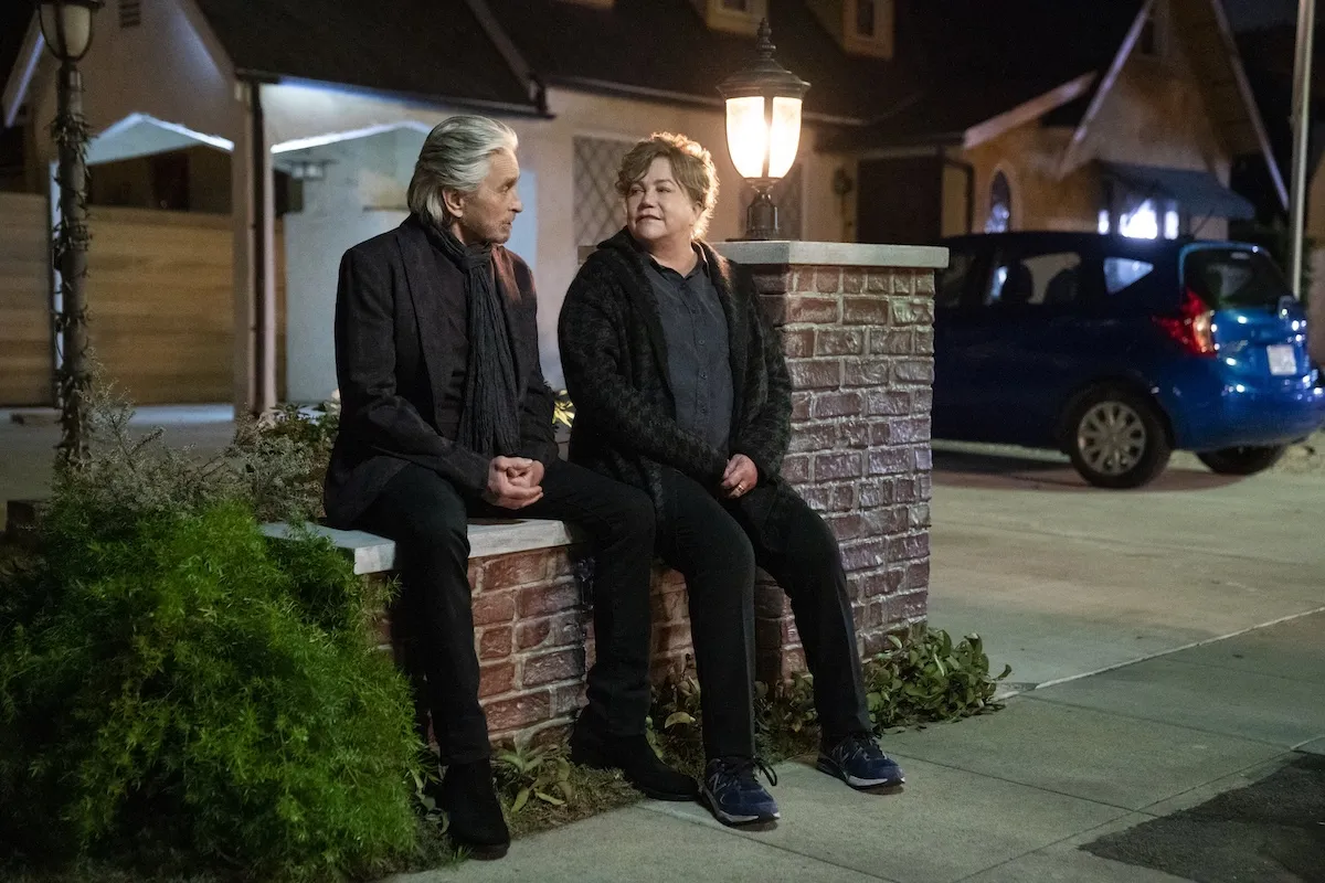 Michael Douglas and Kathleen Turner sitting on a wall outside of a house in 'The Kominsky Method'